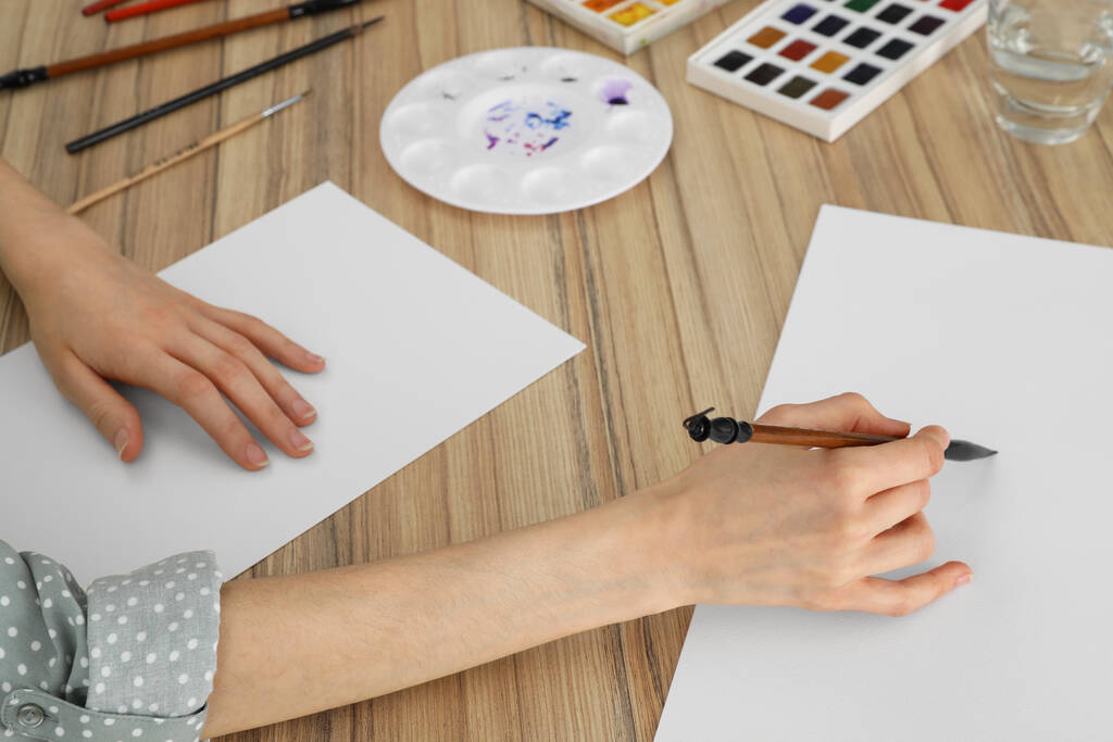 Женщина рисует акварелью на пустой бумаге за деревянным столом, крупным планом - Фото, изображение