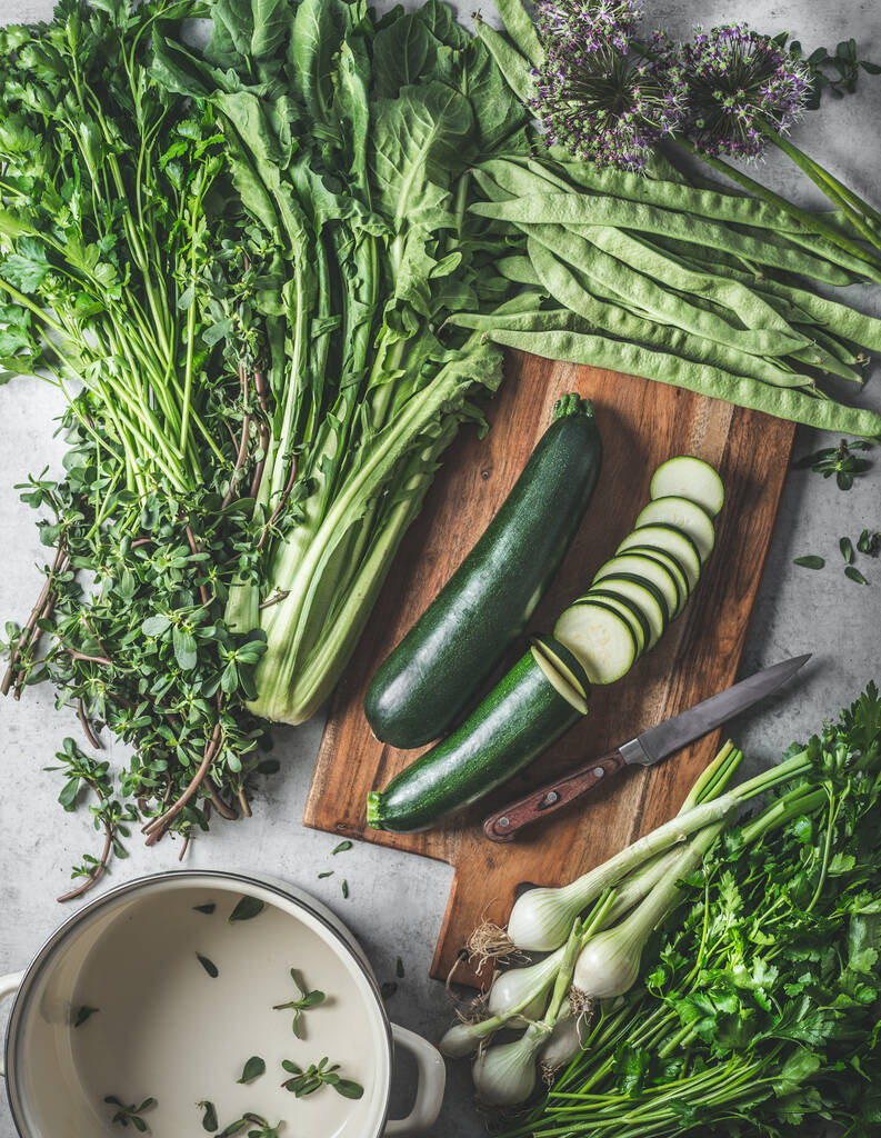 Verduras verdes saludables e ingredientes de hierbas para una sabrosa cocina vegana en la tabla de cortar y la mesa de cocina rústica con olla de cocina vacía. Vista superior - Foto, Imagen