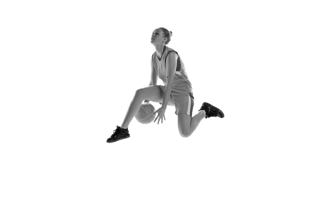 Černobílý obraz mladé atletické dívky hrající, trénink basketbal na bílém pozadí studia. Pojetí profesionálního sportu, koníčku, zdravého životního stylu, akce a pohybu - Fotografie, Obrázek