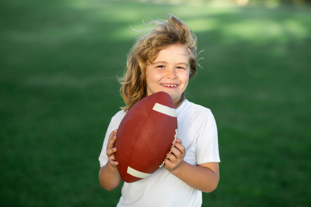 Enfant sportif. Un garçon américain jouant au football américain ou au rugby dans un parc. Des gamins sportifs. Joueur de football tenant le ballon - Photo, image