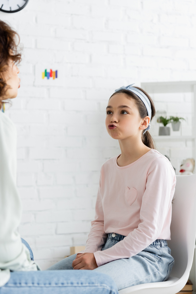 Preteen girl pouting lips during lesson with speech therapist in consulting room  - Photo, Image