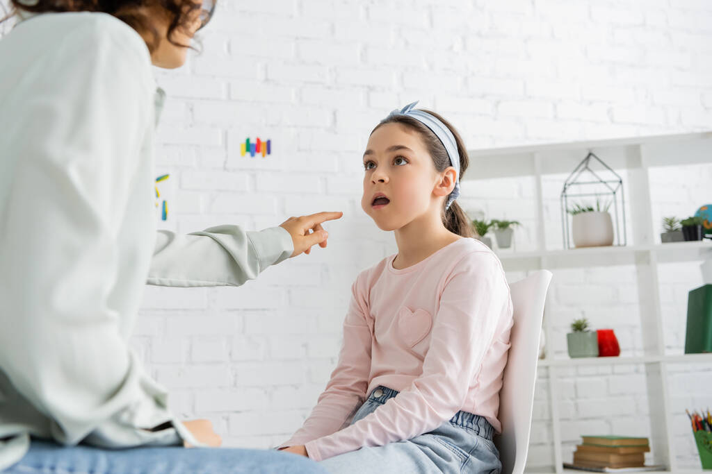 Terapeuta del habla señalando la mejilla de la niña preadolescente en la sala de consulta  - Foto, Imagen
