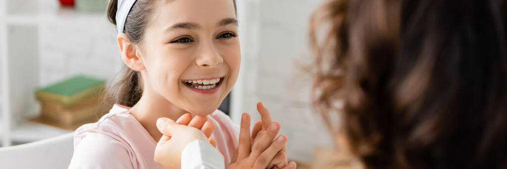 Позитивный ребенок разговаривает с размытым логопедом в консультационной, баннер  - Фото, изображение