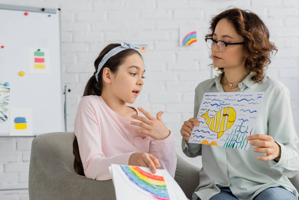 Předdospívající dítě mluví, zatímco psycholog drží kreslení v poradně  - Fotografie, Obrázek