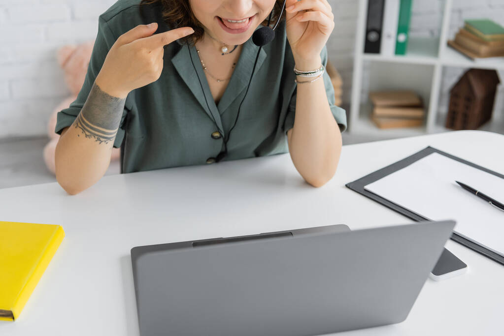 Обрезанный взгляд логопеда, указывающего на язык во время видеозвонка на ноутбуке в консультационной комнате  - Фото, изображение