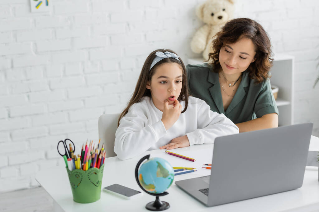 Θετική γυναίκα ψάχνει σε προεφηβική κόρη μιλάμε κατά τη διάρκεια του μαθήματος λογοθεραπείας στο φορητό υπολογιστή στο σπίτι  - Φωτογραφία, εικόνα