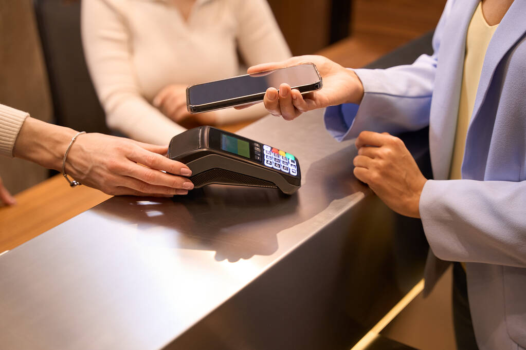 Vista cortada na mão de funcionária auxiliando cliente vestindo jaqueta moderna com transação NFC no check-in mesa - Foto, Imagem