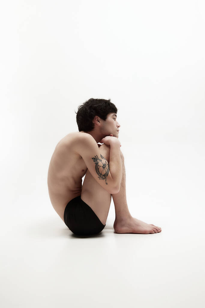 Cítím se osamělý. Studio portrét mladého muže pózujícího bez košile, ve spodním prádle, sedícím na podlaze na bílém pozadí. Pojetí mužské tělo estetika, styl, móda, zdraví, mužská krása, psychologie - Fotografie, Obrázek