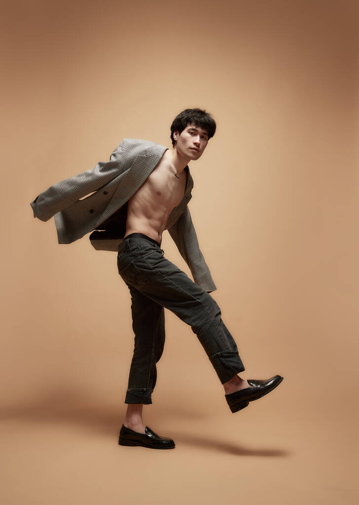 Modern divat. Fiatal ázsiai fickó pózol stílusos szürke dzsekiben és nadrágban stúdió háttérrel. Segélytest alakja. Fogalom férfi test esztétika, stílus, egészség, férfi szépség és divat - Fotó, kép