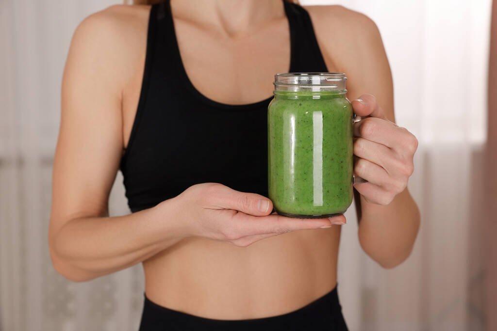 Young woman in sportswear with mason jar of fresh smoothie at home, closeup - Photo, Image