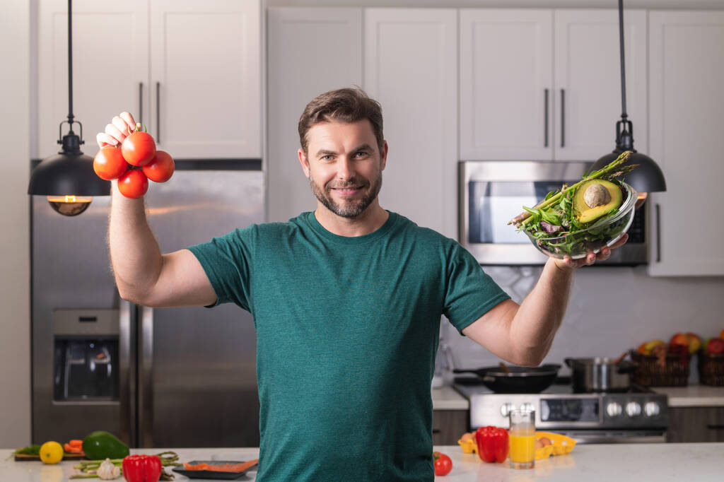 Człowiek z sałatką warzywną w kuchni. Człowiek gotowanie wegańskie zdrowej sałatki w kuchni. Mężczyzna w nowoczesnej kuchni z warzywami, przygotować świeżą sałatkę warzywną na obiad lub obiad. Zdrowy obiad lub kolacja - Zdjęcie, obraz