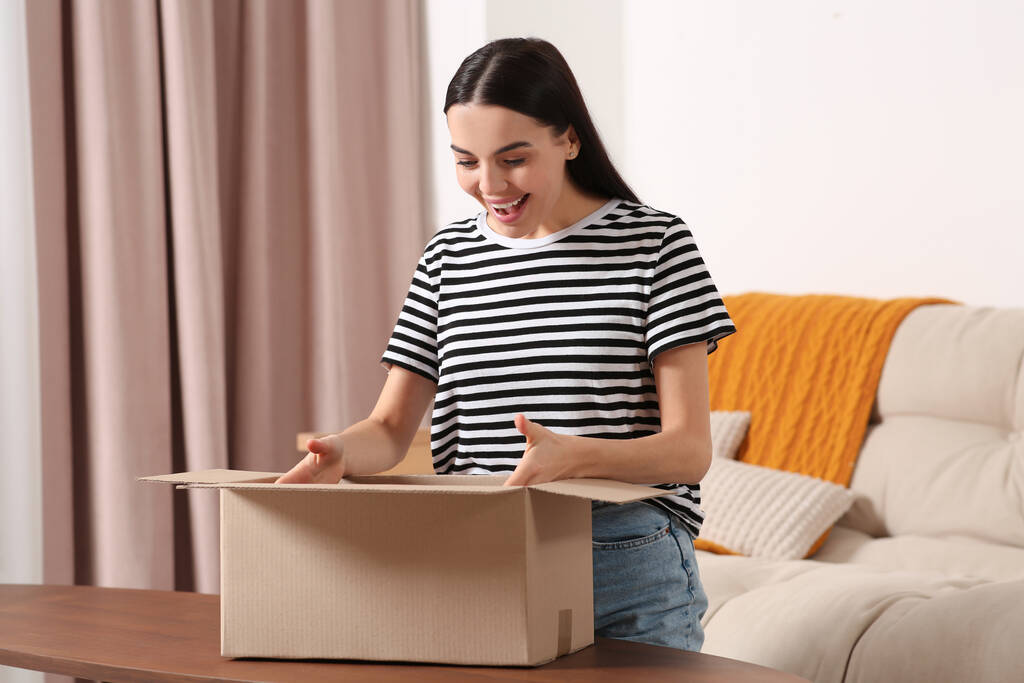 Érzelmes fiatal nő nyitja ki a csomagot otthon. Internetes vásárlás - Fotó, kép