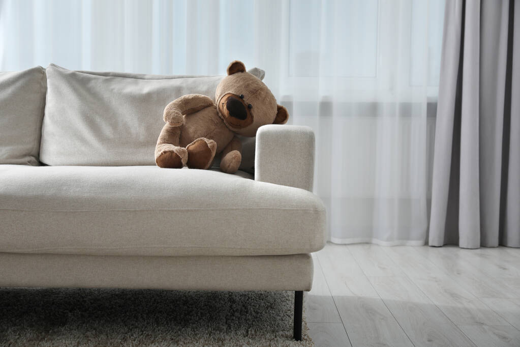 Bonito oso de peluche solitario en el sofá en la habitación. Espacio para texto - Foto, Imagen