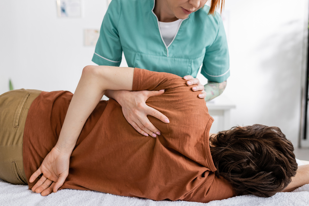 physiotherapist massaging painful shoulder of man in rehabilitation center - Photo, Image