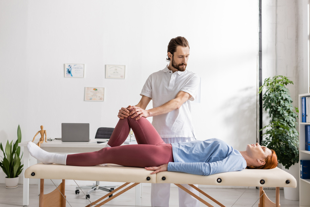 thérapeute manuel barbu faisant massage du genou à la femme dans le centre de réadaptation - Photo, image