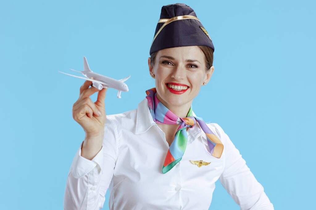 χαρούμενη μοντέρνα αεροσυνοδός γυναίκα σε μπλε φόντο με στολή με ένα μικρό αεροπλάνο. - Φωτογραφία, εικόνα