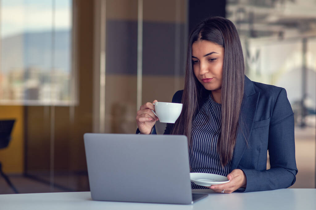 Mujer joven que trabaja en el ordenador portátil y beber café en la oficina. - Foto, imagen