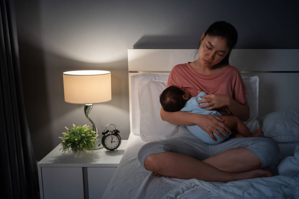 眠くて疲れた母親が夜のベッドで新生児を母乳で育て - 写真・画像