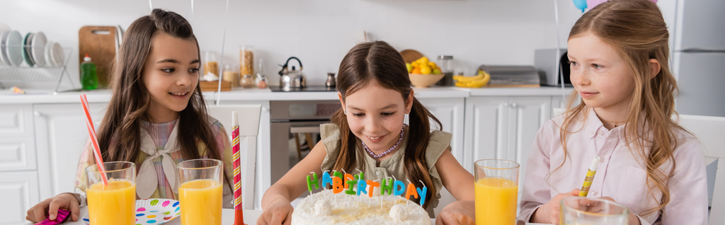 chica feliz mirando pastel de cumpleaños con velas cerca de amigos durante la celebración en casa, pancarta  - Foto, Imagen