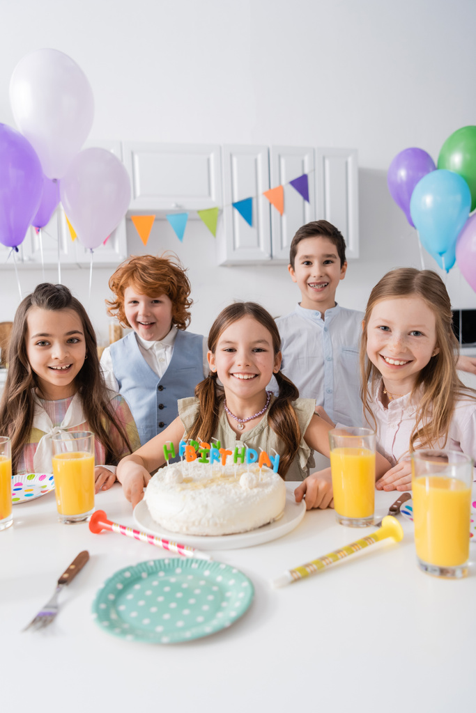 группа счастливых мальчиков и девочек, празднующих день рождения рядом с вкусным тортом дома - Фото, изображение