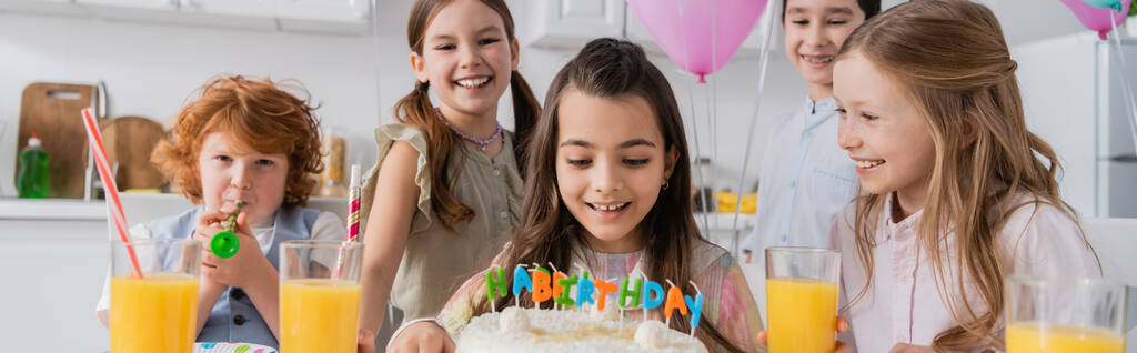 veselá dívka při pohledu na narozeninový dort v blízkosti šťastných přátel během párty doma, banner  - Fotografie, Obrázek