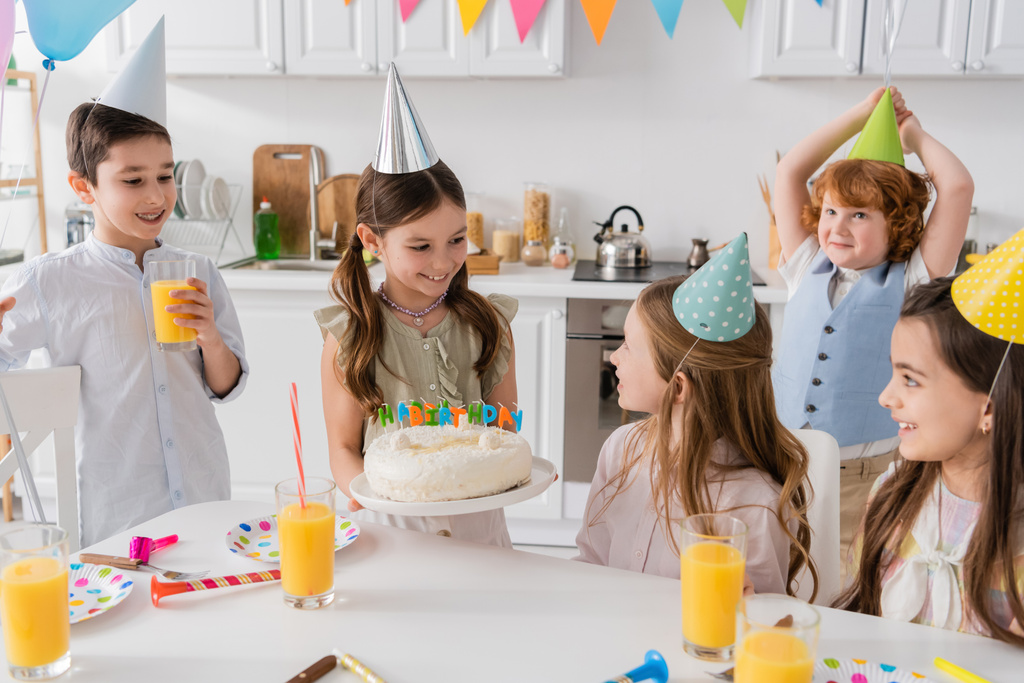 menina feliz segurando bolo de aniversário com velas perto de amigos alegres durante a festa em casa   - Foto, Imagem