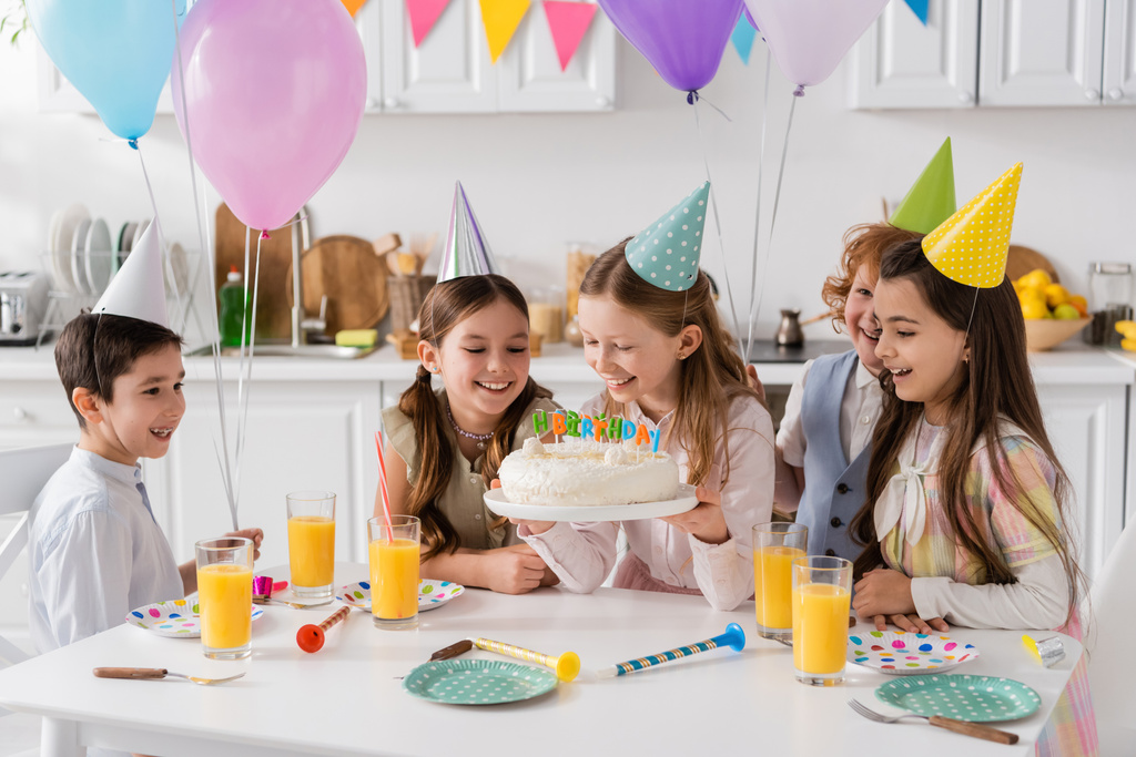 счастливая девушка с тортом на день рождения со свечами возле веселых друзей во время празднования дома   - Фото, изображение