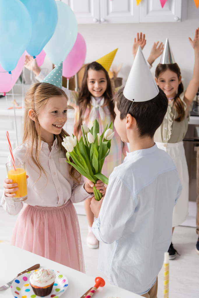feliz chica con vaso de jugo tomando tulipanes de chico cerca de amigos en fondo borroso  - Foto, Imagen