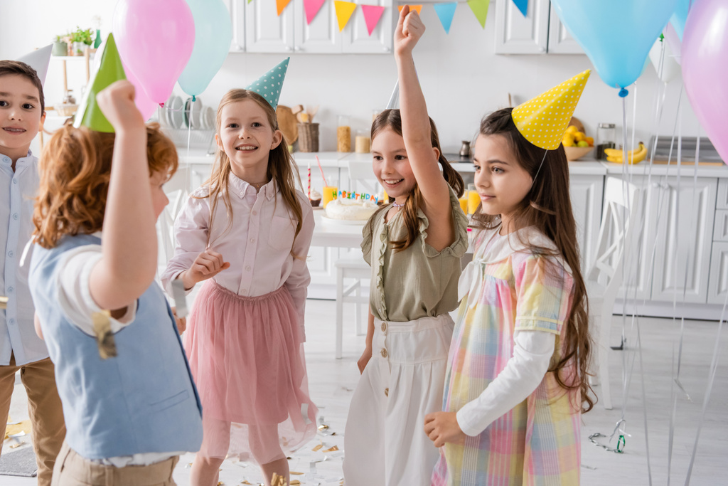 パーティーキャップの幸せな子供たちのグループは自宅で誕生日のお祝いの間に踊る  - 写真・画像