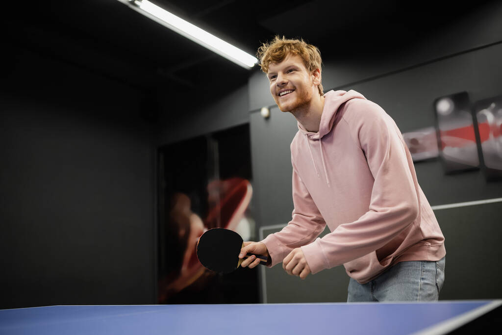 Веселый рыжий мужчина играет в настольный теннис в игорном клубе  - Фото, изображение