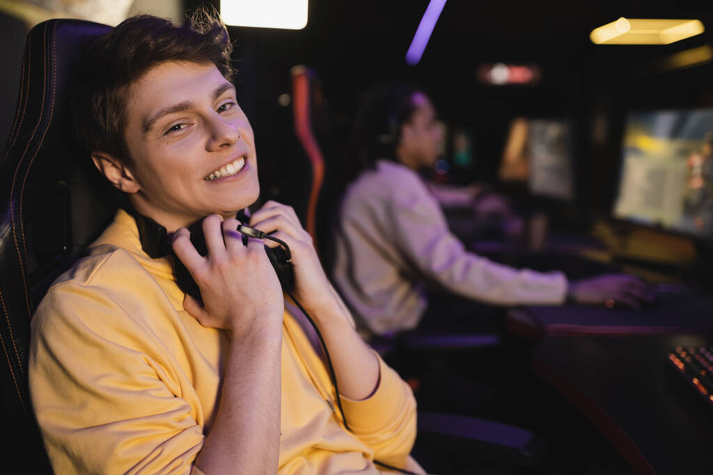 Zorgeloze jonge man met een koptelefoon en kijken naar de camera in cyber club  - Foto, afbeelding