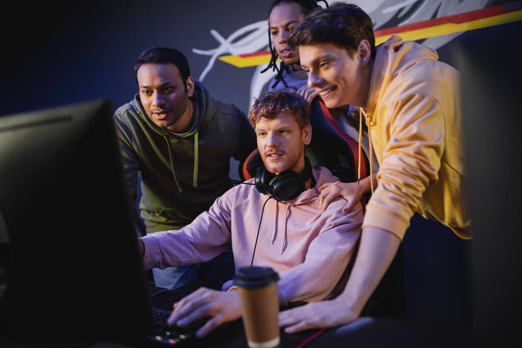 Χαρούμενοι πολυεθνικοί άνδρες που κοιτάζουν φίλους που παίζουν βιντεοπαιχνίδια στον υπολογιστή στο gaming club  - Φωτογραφία, εικόνα