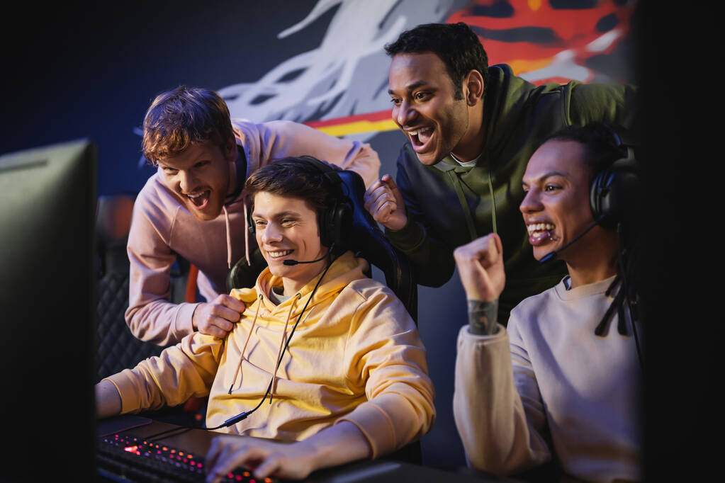 Aufgeregt interrassische Männer betrachten Freund beim Spielen von Videospielen auf dem Computer in einem Spielclub  - Foto, Bild