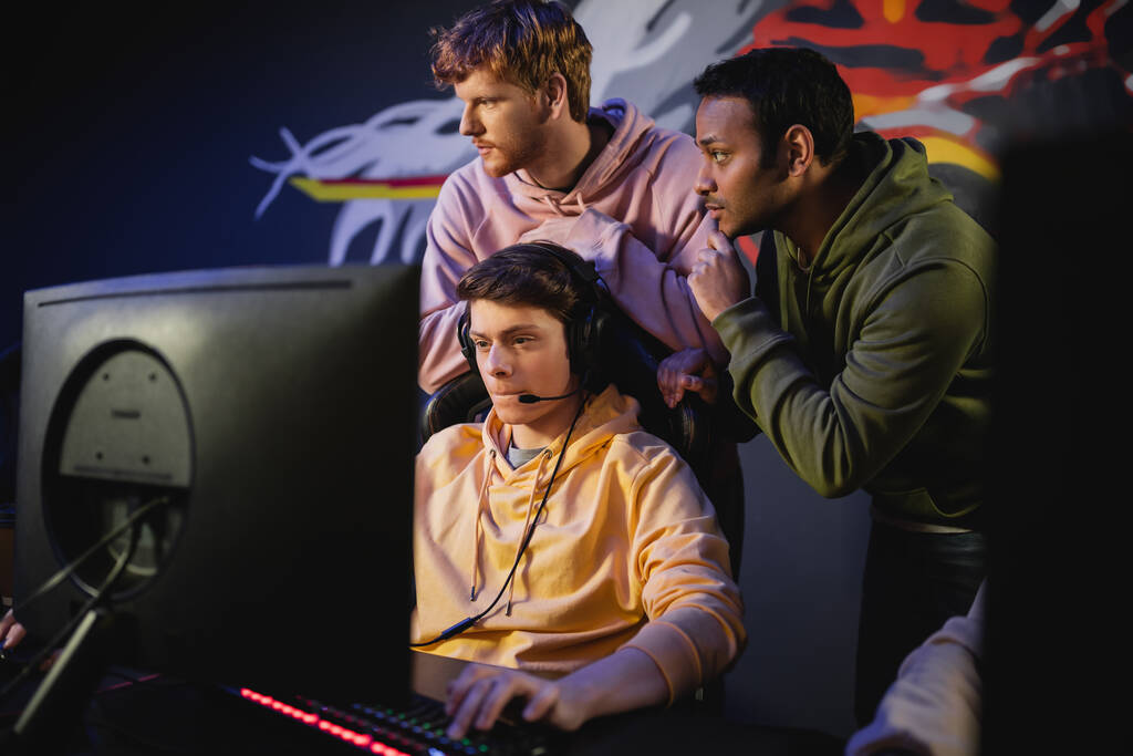 Siber kulüpte bilgisayar başında bilgisayar oyunu oynayan oyuncunun yanında duran ırklar arası bir takım.  - Fotoğraf, Görsel