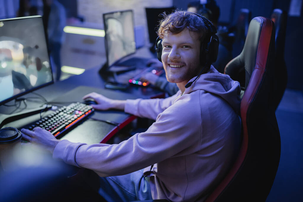 Usmívající se hráč dívá na kameru při hraní videohry v kybernetickém klubu  - Fotografie, Obrázek