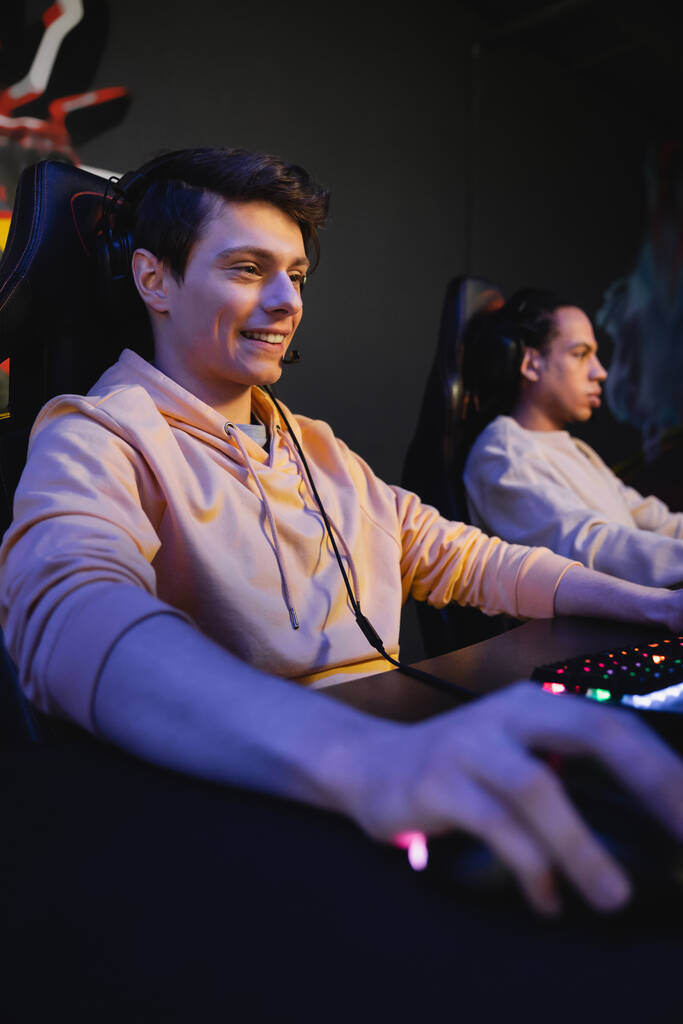 Giocatore sorridente con cuffie seduto vicino alla tastiera nel cyber club  - Foto, immagini