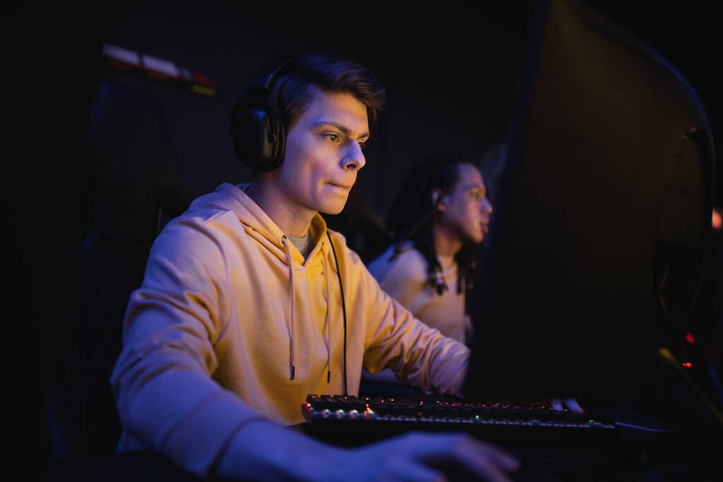 Mladý muž ve sluchátkách hrát počítačovou hru v kybernetickém klubu s osvětlením  - Fotografie, Obrázek