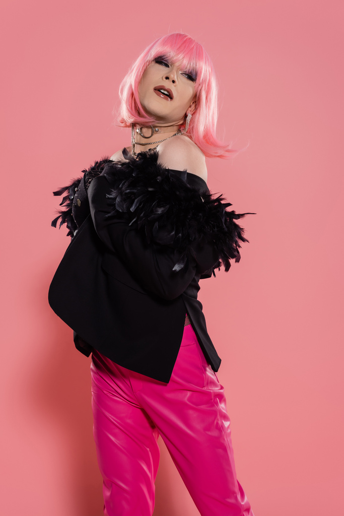 Goed gekleed drag queen in pruik en jasje weg te kijken terwijl poseren op roze achtergrond  - Foto, afbeelding
