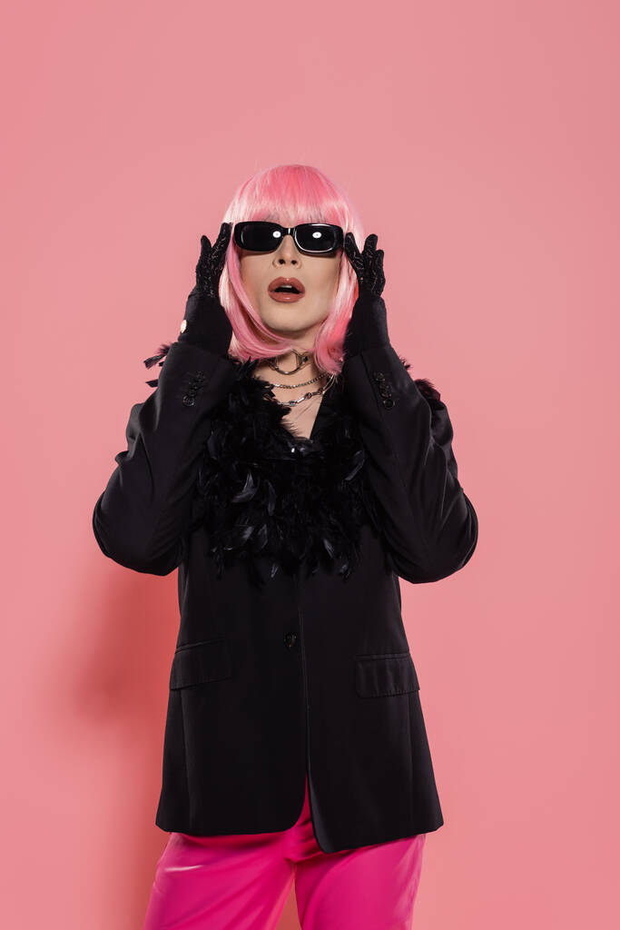 Перетащите королеву в парике и пиджаке касаясь солнцезащитных очков на розовом фоне  - Фото, изображение