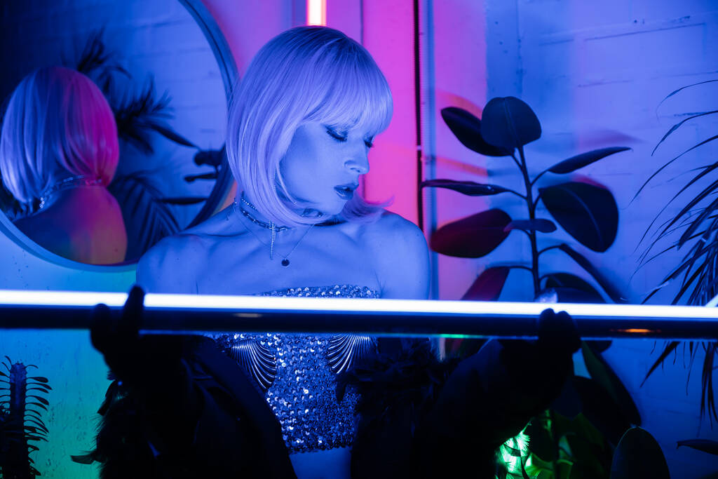 Trendy drag queen en peluca y lámpara de neón de celebración superior en casa  - Foto, Imagen