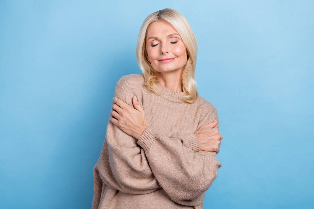 Foto anuncio bandera de la señora pensionista modelo desgaste suéter beige de moda abrazándose ropa fresca aislada sobre fondo de color azul. - Foto, imagen