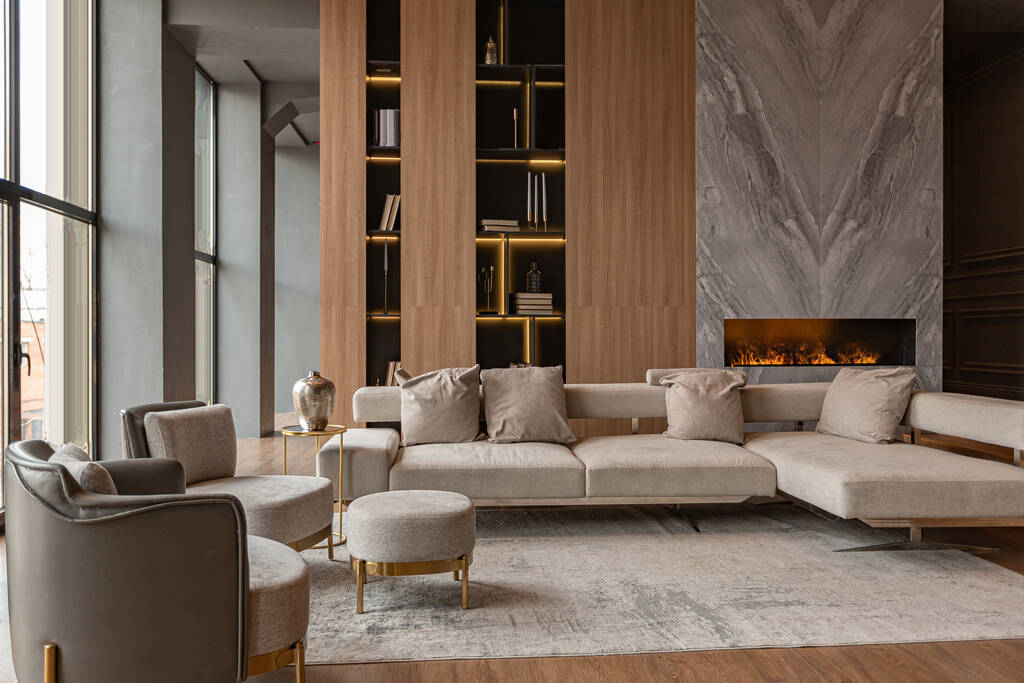 リビングルーム、大理石の壁の暖炉と金の要素を持つ光、灰色の家具を主導したモダンなデザインの高級カントリーハウスのシックな高価なインテリアでスタイリッシュな本棚 - 写真・画像