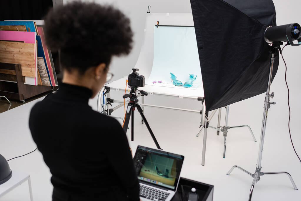 πίσω όψη του Αφροαμερικανού διαχειριστή περιεχομένου που εργάζεται σε laptop στο φωτογραφικό στούντιο - Φωτογραφία, εικόνα