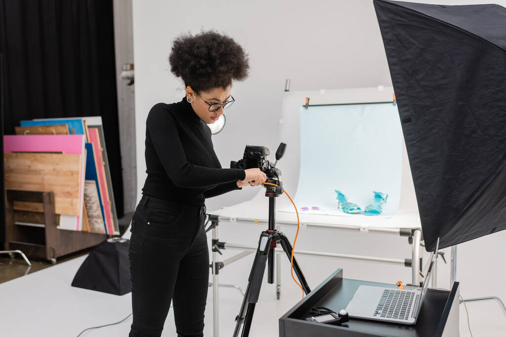 Afrikanisch-amerikanischer Content-Produzent verbindet Digitalkamera mit Laptop in modernem Fotostudio - Foto, Bild