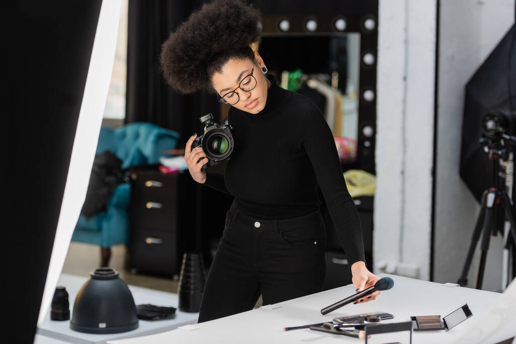 afro-amerikai tartalomkészítő digitális fényképezőgép és kozmetikai kefe közelében forgatóasztal fotó stúdió - Fotó, kép