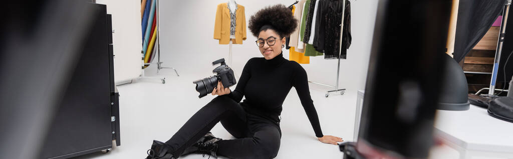 allegro produttore di contenuti africani americani con fotocamera digitale seduto in moderno studio fotografico, banner - Foto, immagini