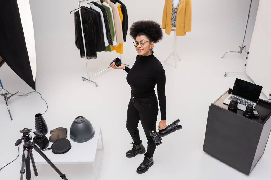 magas látószögű kilátás boldog afro-amerikai fotós gazdaság digitális fényképezőgép és fotópont közelében stílusos ruhák fotó stúdió - Fotó, kép