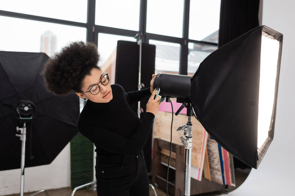 afrikkalainen amerikkalainen sisällöntuottaja silmälasien kanssa softbox heijastin valokuva studio - Valokuva, kuva