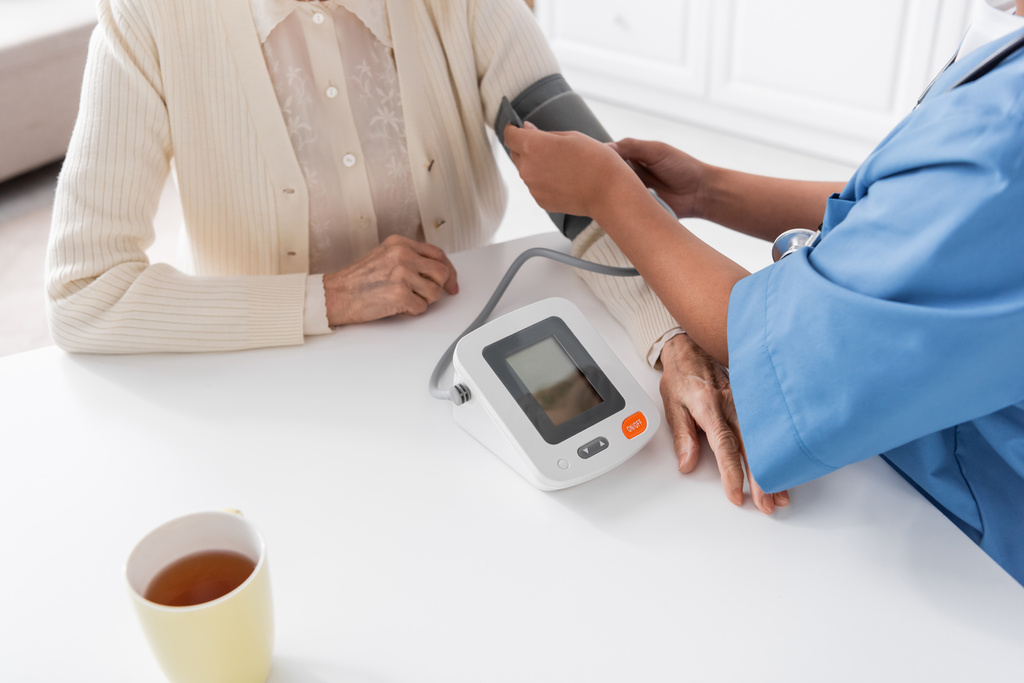 обрізаний вид багаторасової медсестри, що вимірює кров'яний тиск старшої жінки
  - Фото, зображення