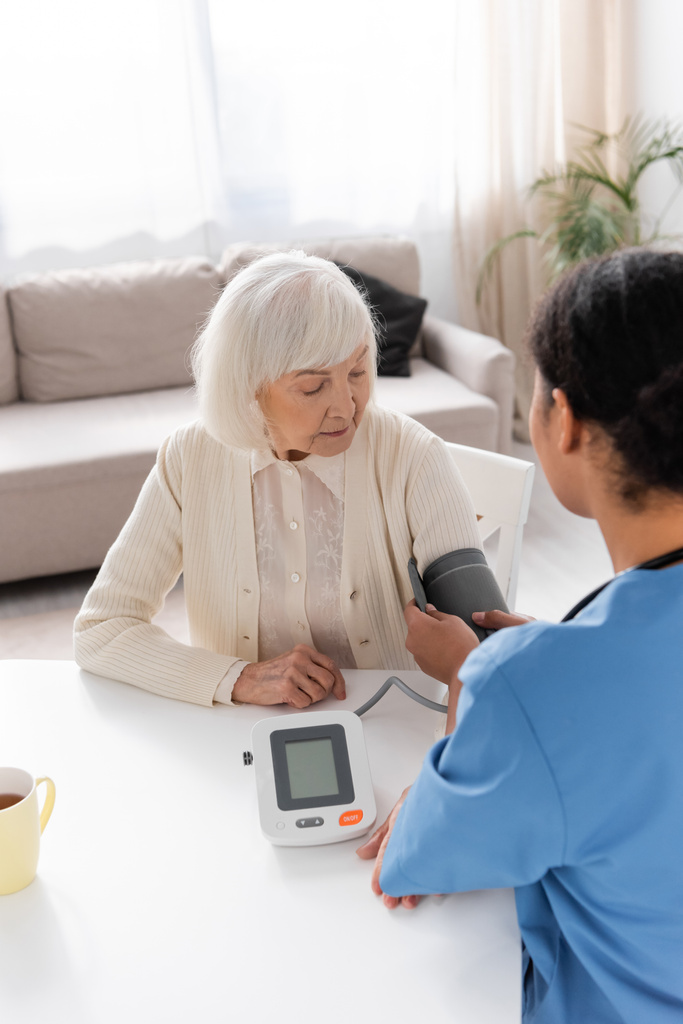 monirotuinen sairaanhoitaja, joka mittaa eläkkeelle jääneen harmaahiuksisen naisen verenpainetta  - Valokuva, kuva